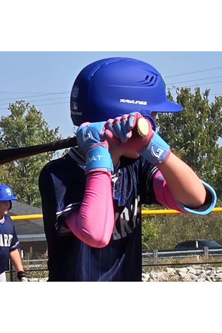 Young baseball player wearing GOAT batting gloves and a blue helmet, gripping a bat in a ready stance on the field.