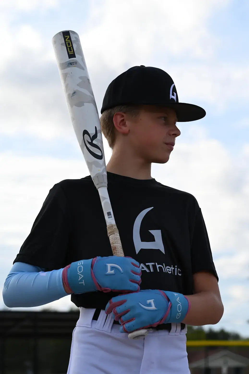 Youth baseball player wearing GOAThletic blue arm compression sleeve and batting gloves holding bat