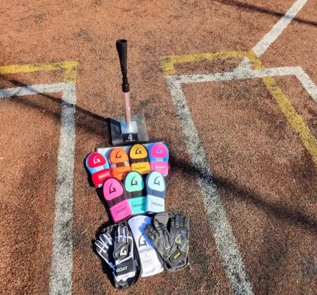 GOAThletic product collection flat lay on baseball field showing batting gloves sliding mitts and batting tee