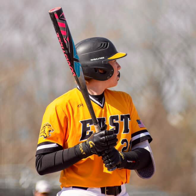 Youth baseball player at bat wearing GOAThletic black batting gloves and arm sleeve in yellow jersey